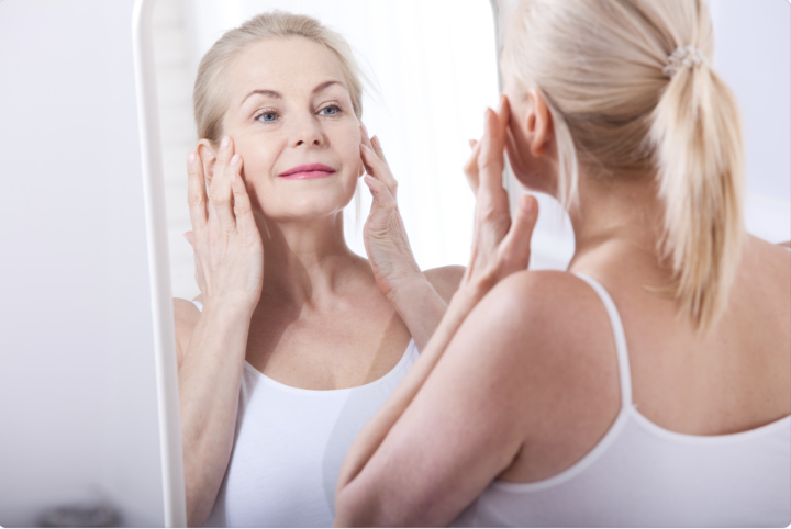 middle aged woman looking at skin in mirror