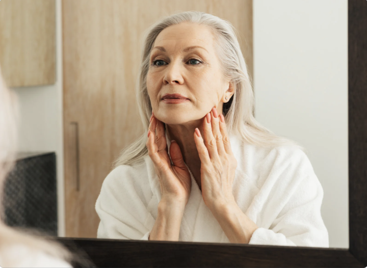 woman gently looking at face in the mirror